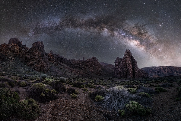 An example of long time exposure photography showing an expansive and rugged desert scene at night with stars in the sky. 