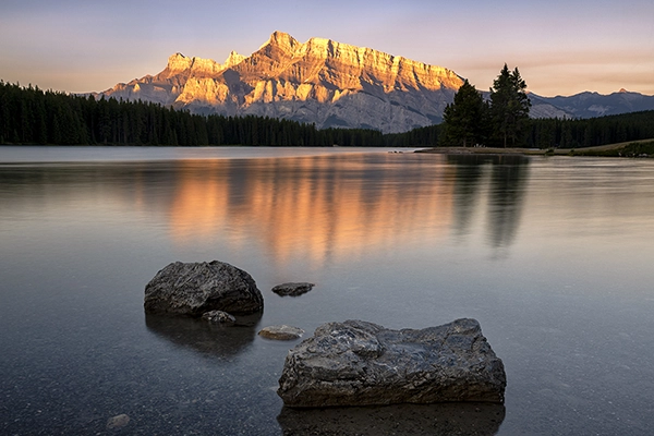 A peaceful lake with undisturbed water reflecting the golden glow of the sun on a majestic mountain range. 