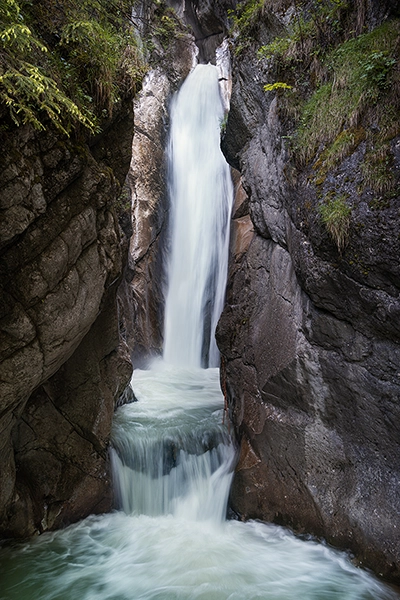A cascading waterfall between two cliffs with greens