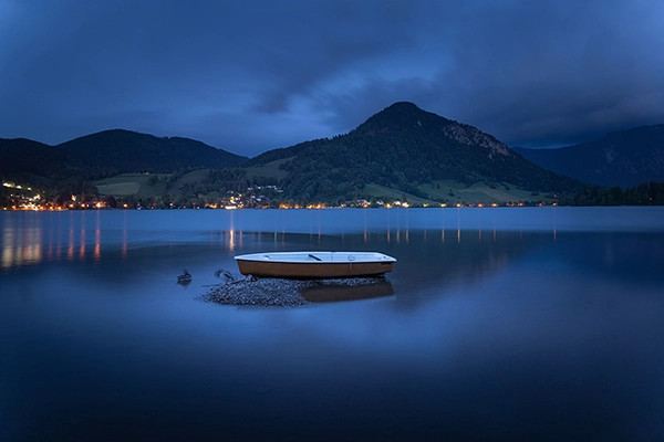 A serene scene example of long exposure shots featuring a small boat resting in a small lake surrounded by rolling hills and mountains at twilight